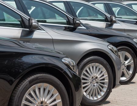 Parked black and gray cars lined up in a row, close-up on the front sides and wheels.