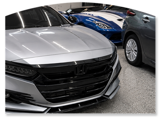 Two silver sedans and a blue sports car parked closely together in a garage