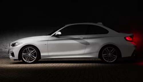 Silver sports coupe in side view on a dark background, with red taillights glowing.