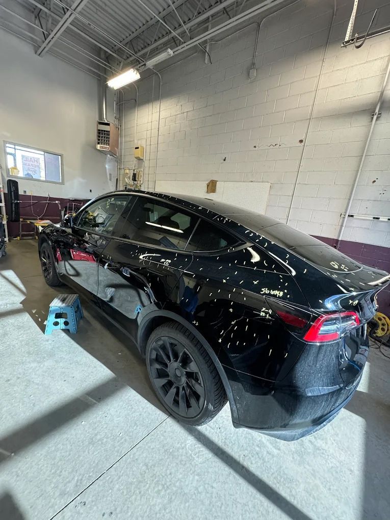 Black Tesla sedan in an auto shop, viewed from the rear side under bright lights.