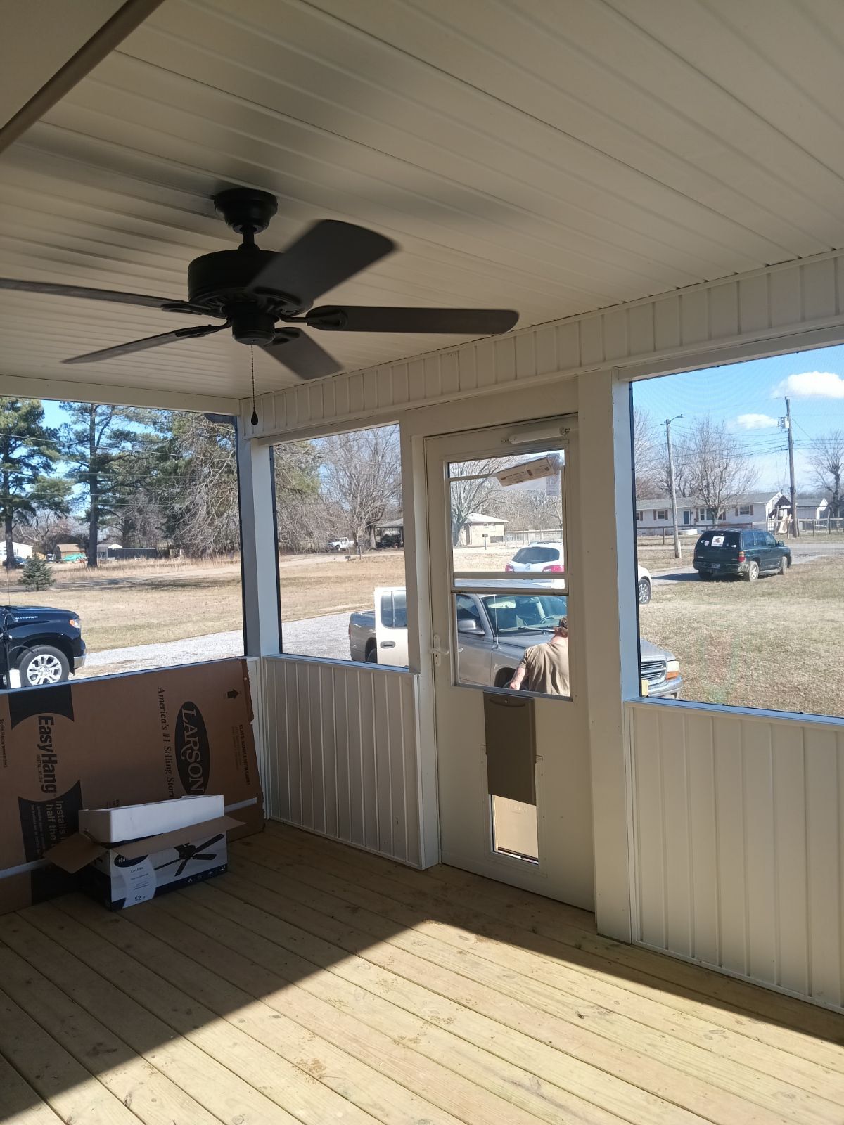 Covered porch with ceiling fan, wooden floor, screened windows, and door.