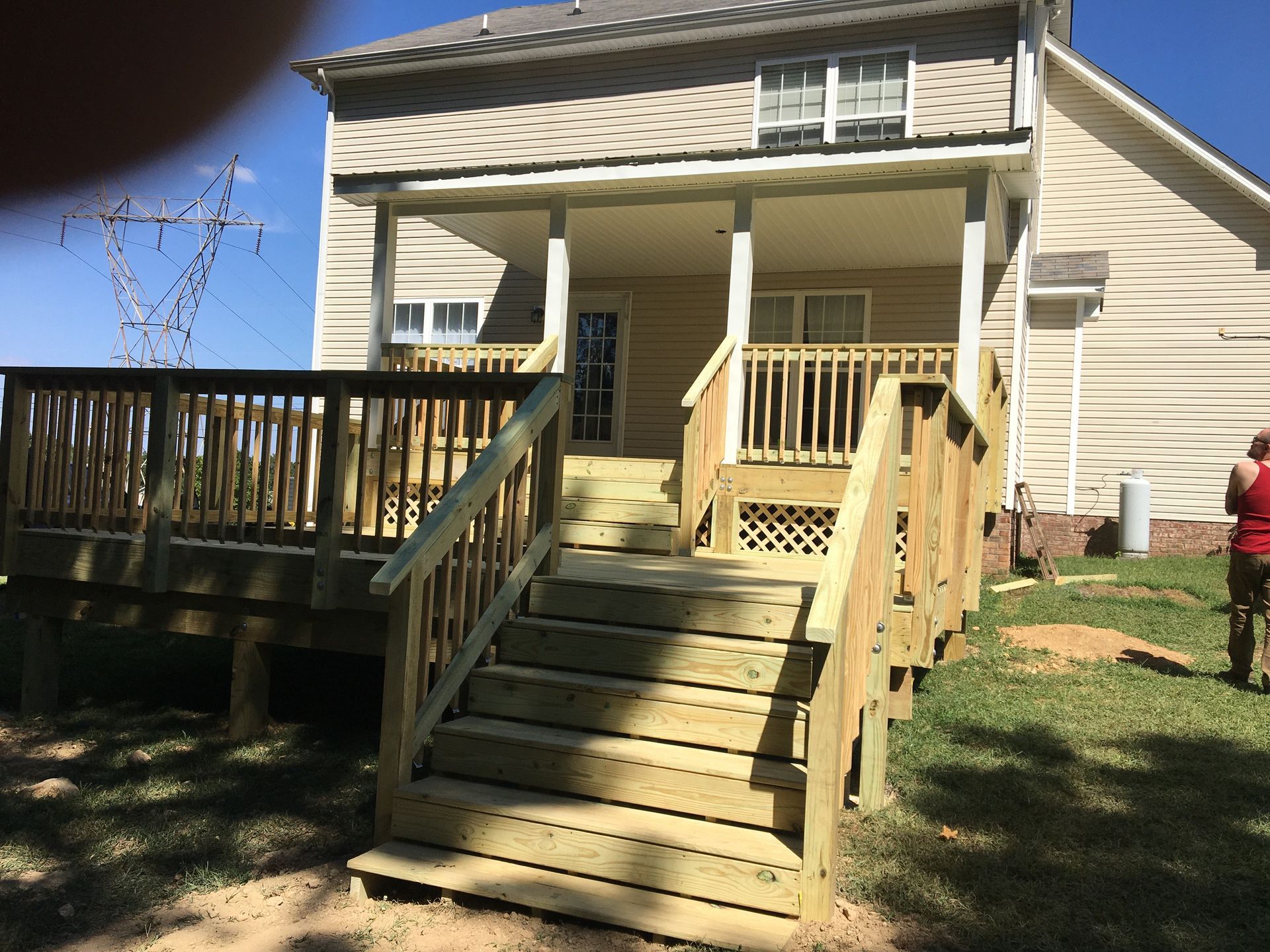 Wooden deck and stairs leading to a covered porch attached to a tan house on a sunny day.