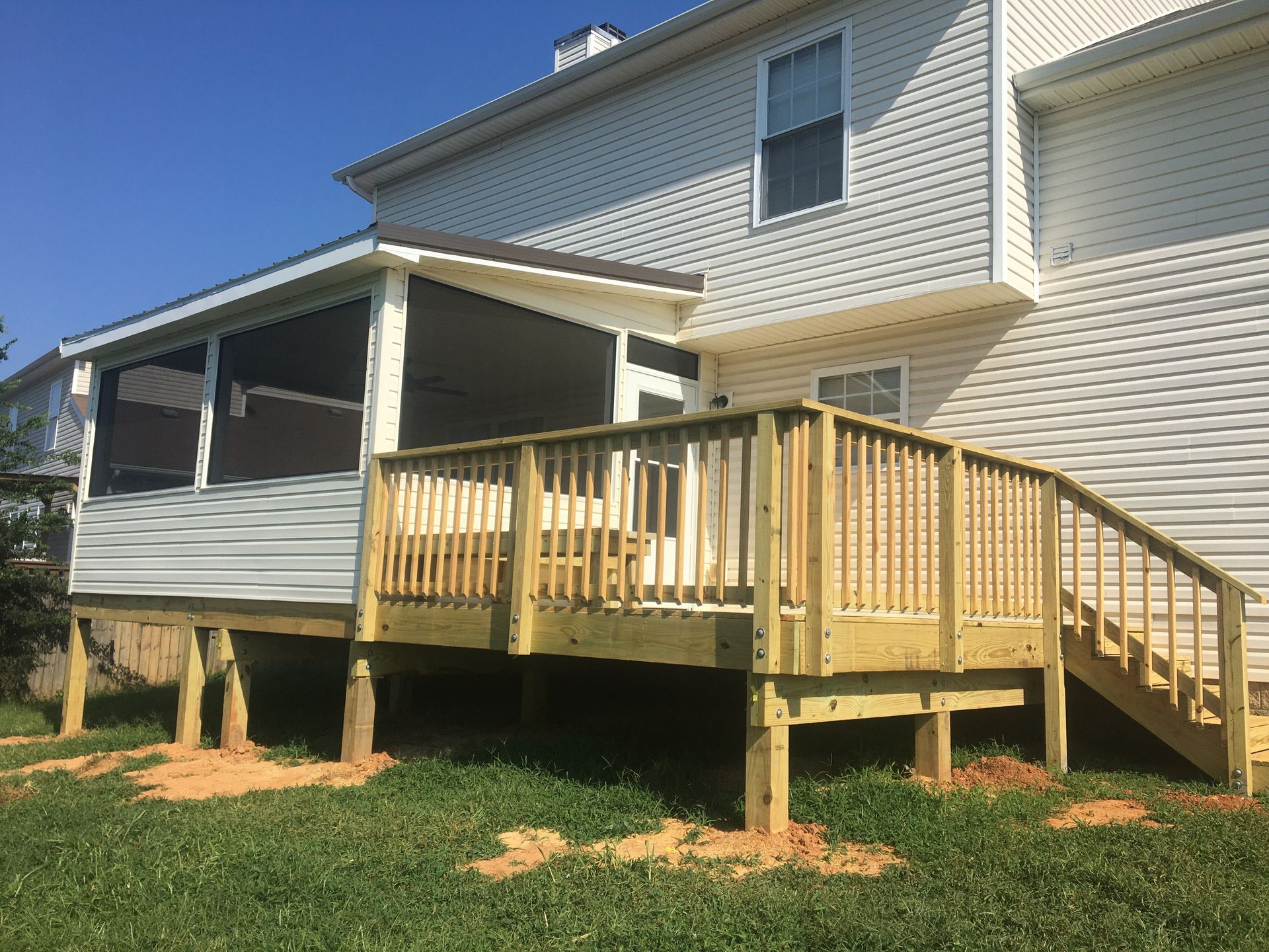 Wooden deck and screened porch attached to a two-story house, set in a grassy yard.