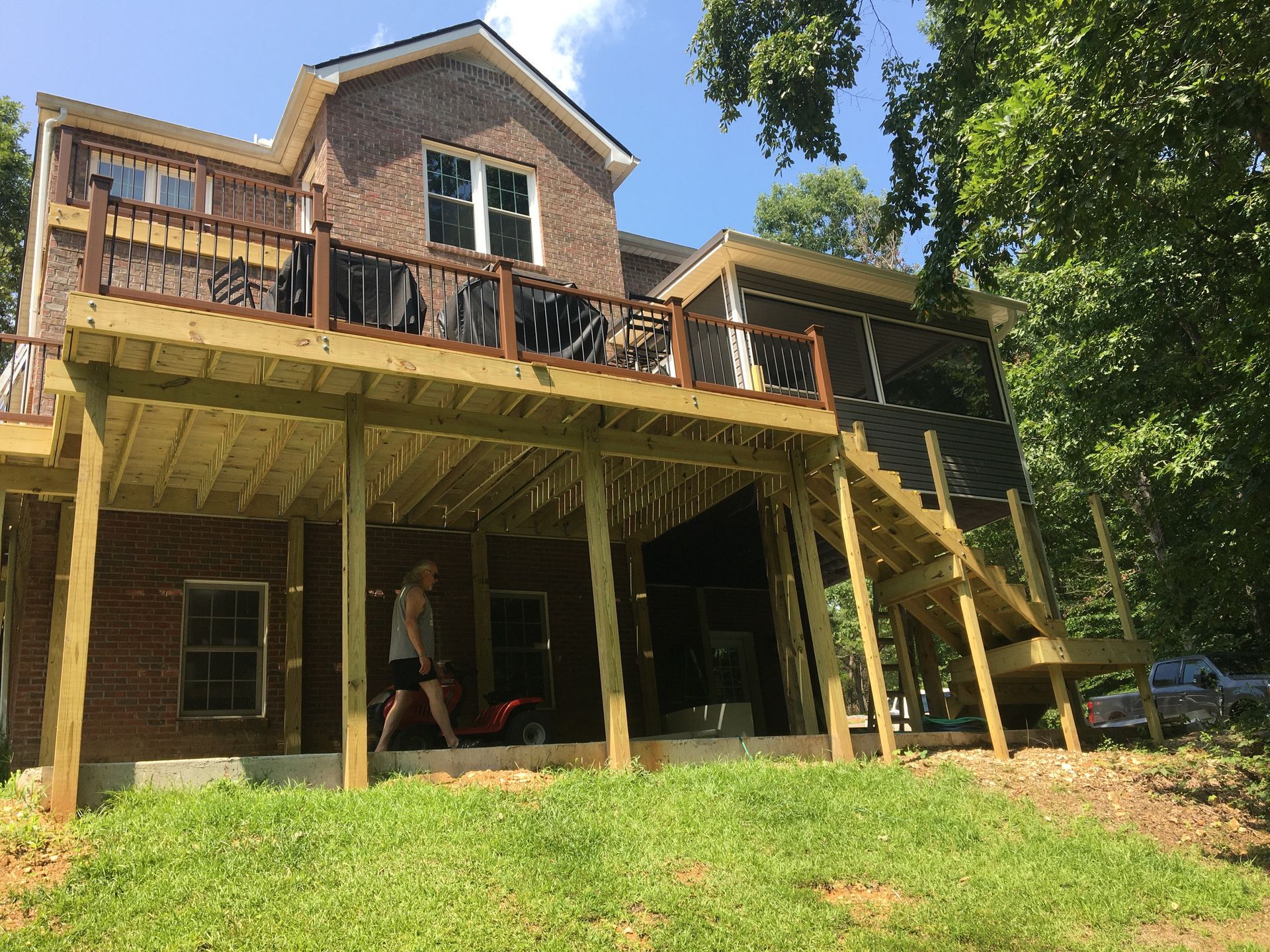 Two-story house with wooden decks. A person walks underneath the deck, grass in the foreground.