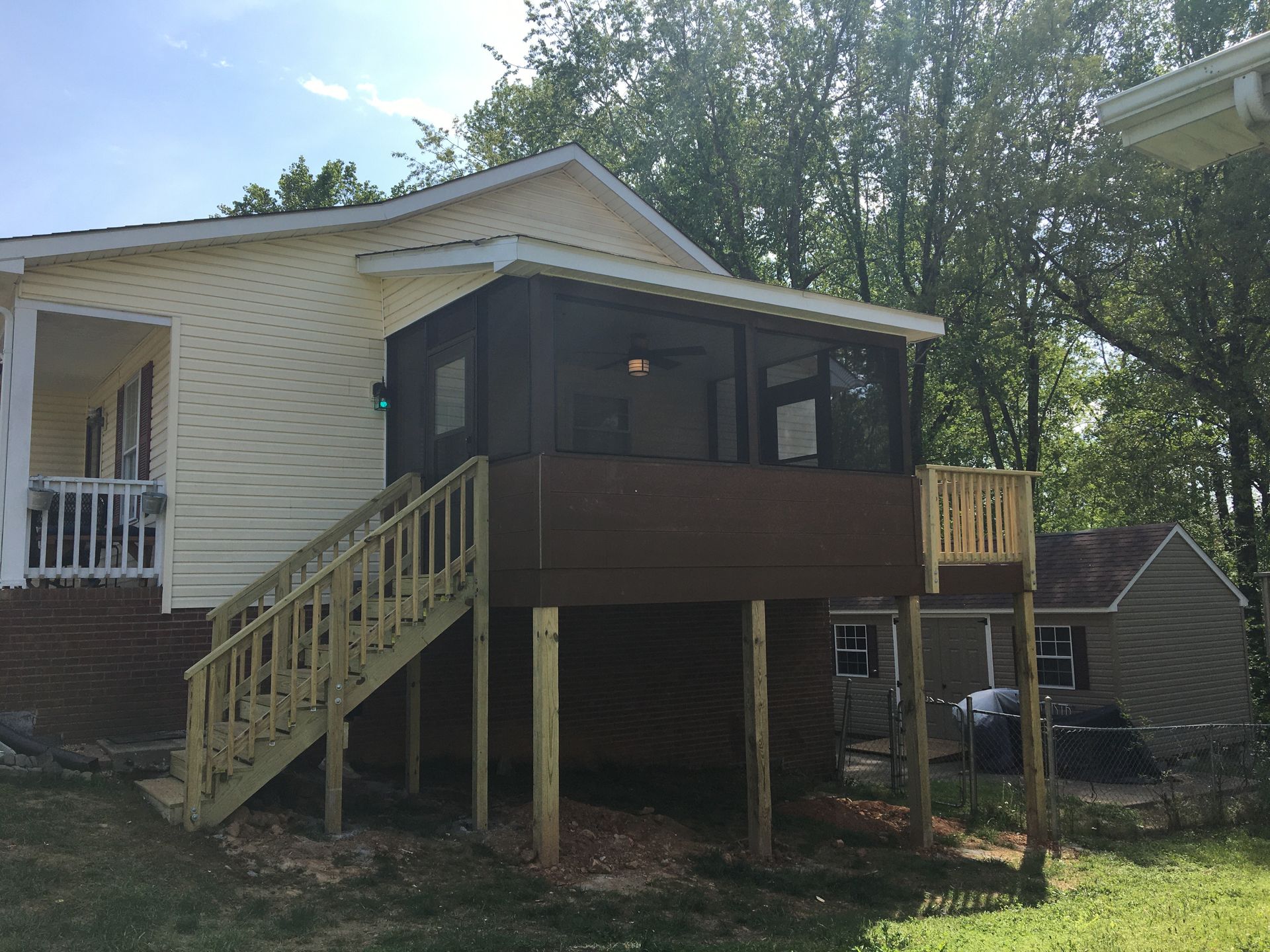 Back of a light yellow house with a brown screened porch and wooden stairs leading up.