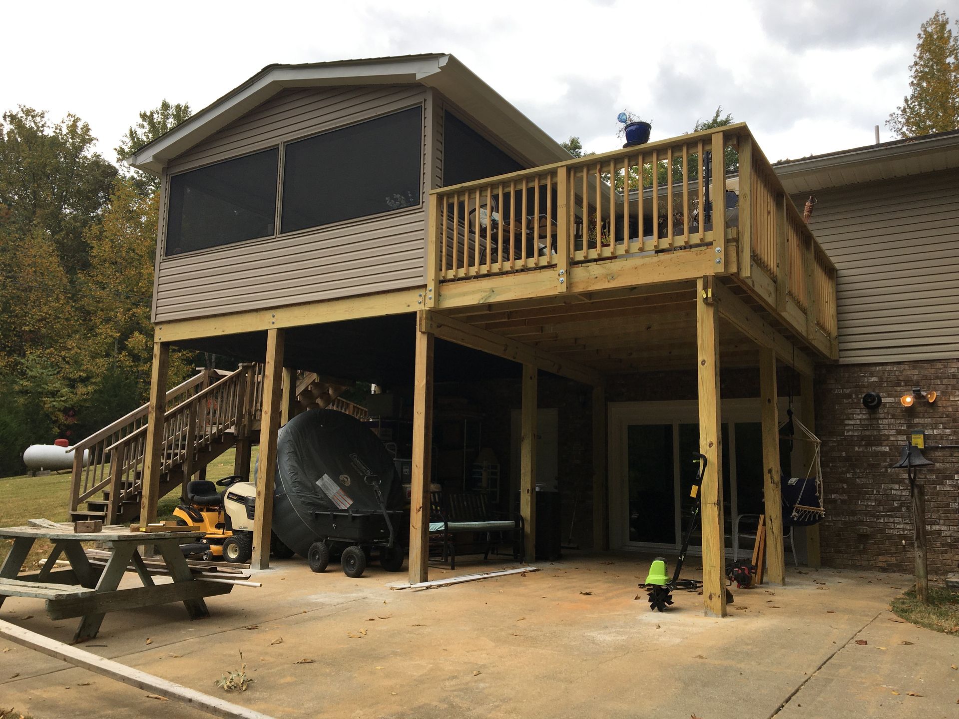 Wooden deck with screened porch, built-in storage, and attached to a house with a concrete patio.