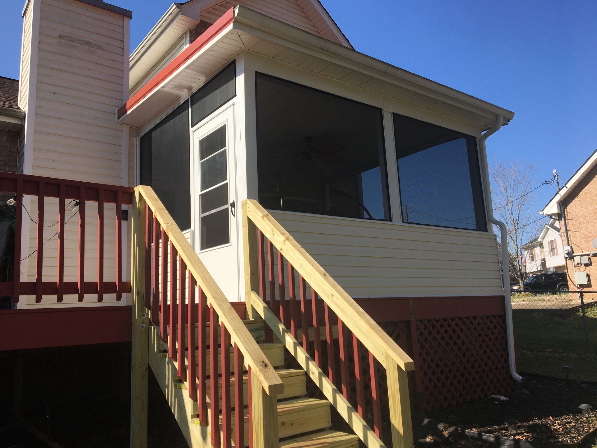 Screened porch with stairs leading up from a wooden deck, against a blue sky.