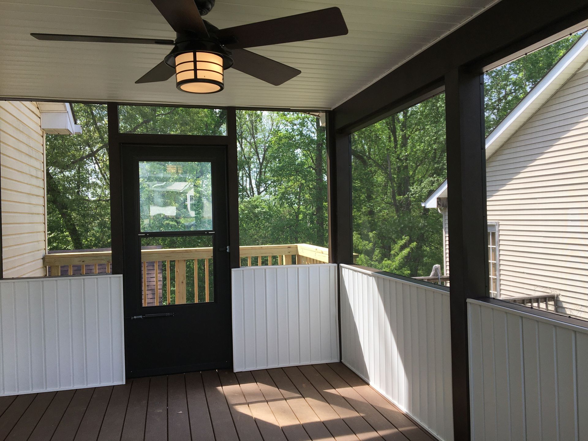 Screened porch with dark trim and ceiling fan, overlooking a wooded area.