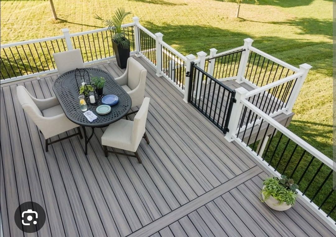 Elevated gray deck with dining table, chairs, and black railing; overlooks green lawn.