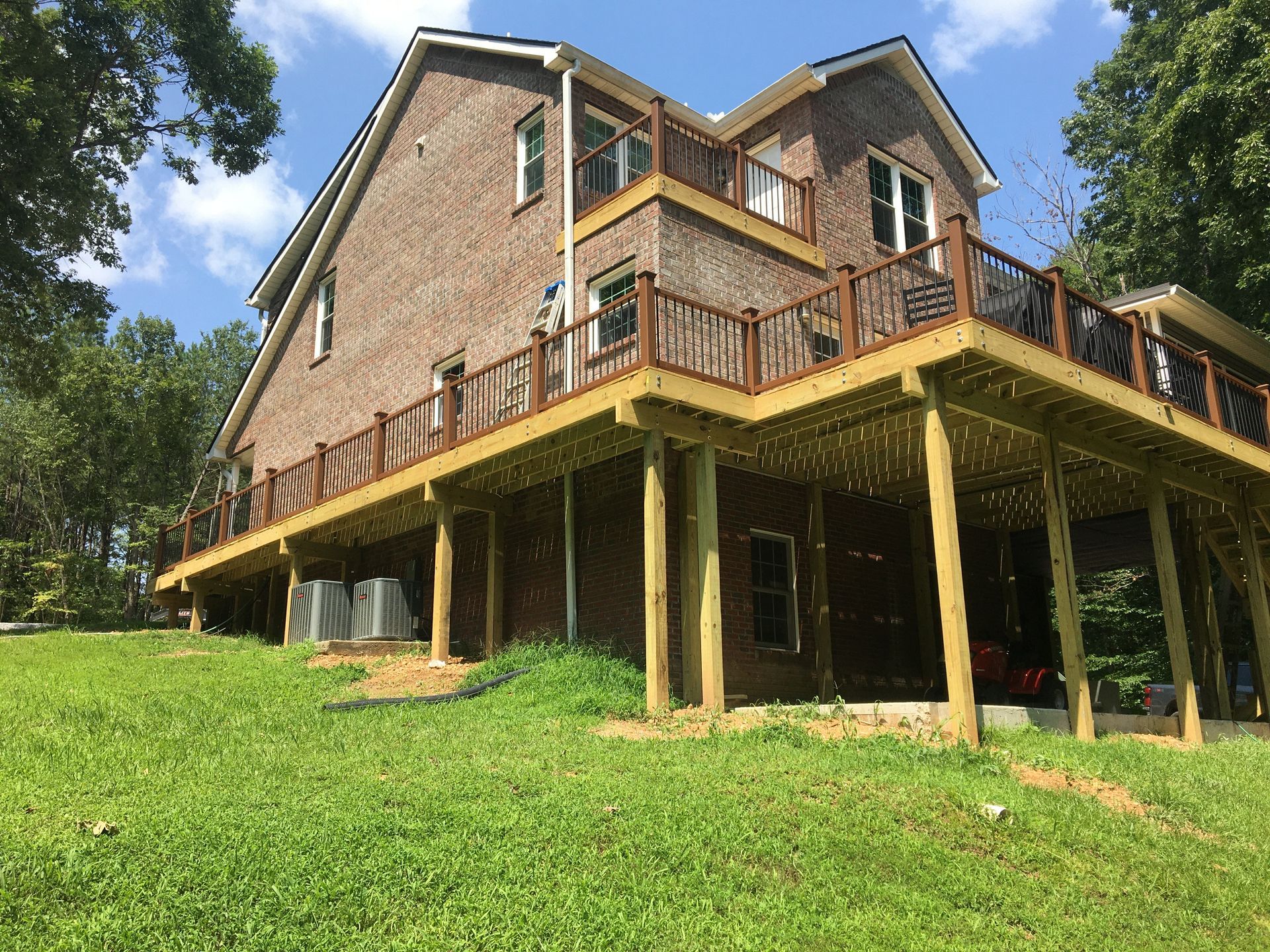 Two-story brick house with large wooden deck. Brown deck and railing with green grass in front.