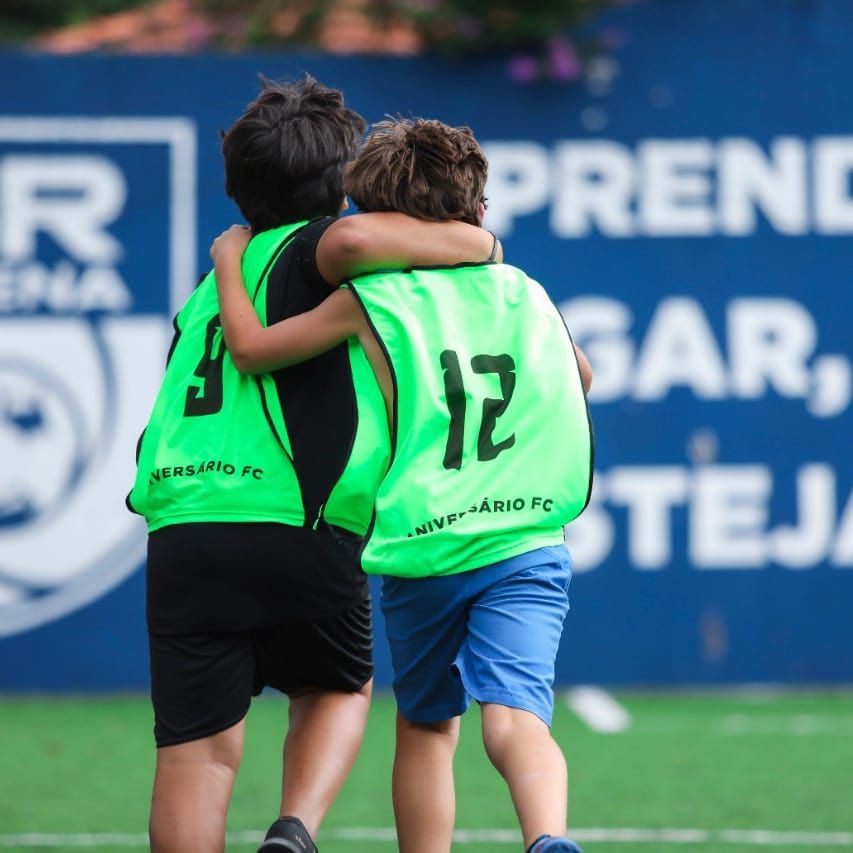 Dois jovens vestindo coletes verdes se abraçam em um campo de futebol.