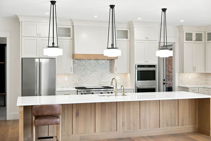 Bright modern kitchen with white cabinets, navy island, gold pendant lights, and stainless steel appliances