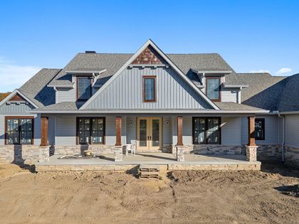 Front view of a gray stone and siding house under construction with unfinished yard and porch columns