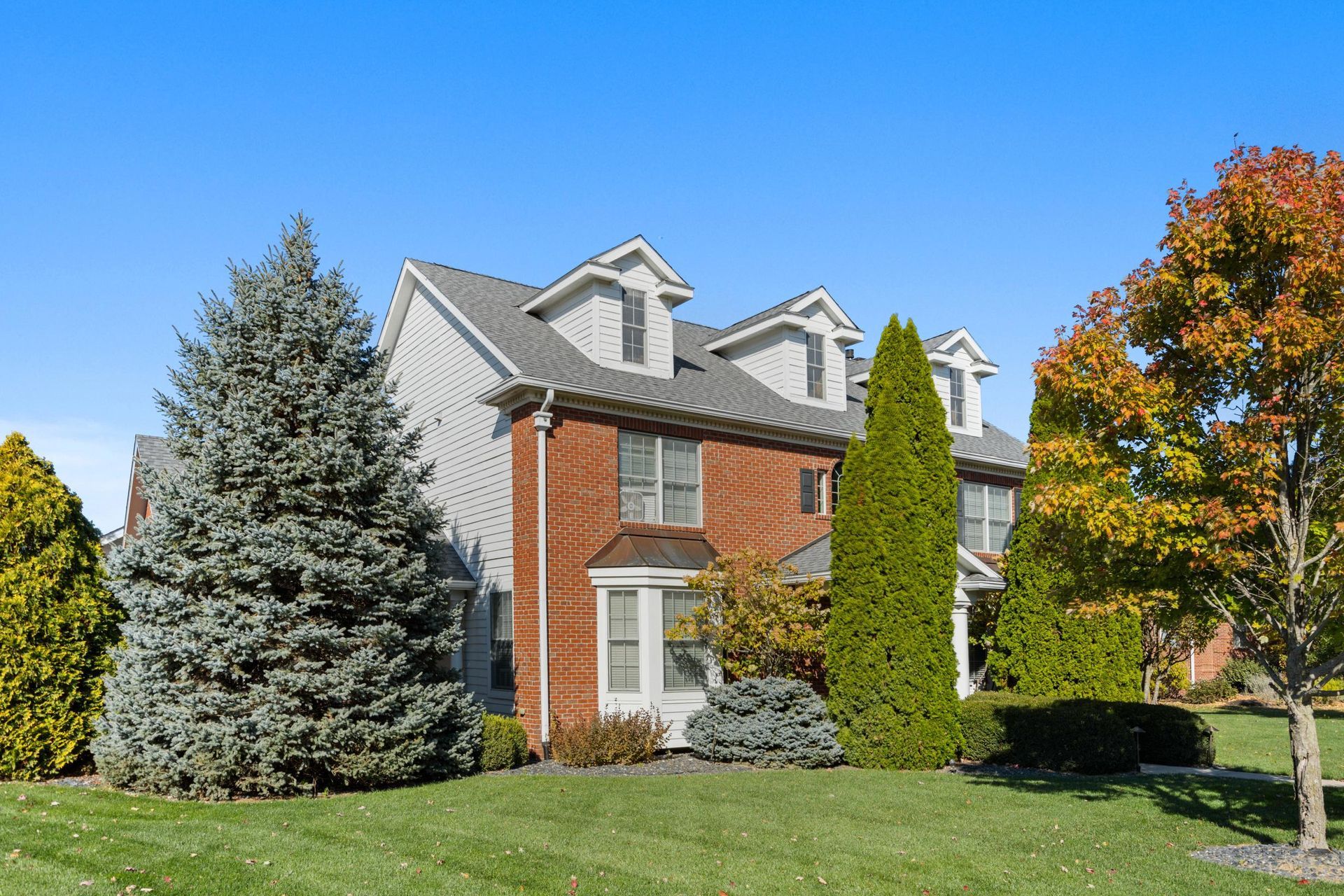 Brick suburban house with gray roof, front lawn, and trees under a bright blue sky