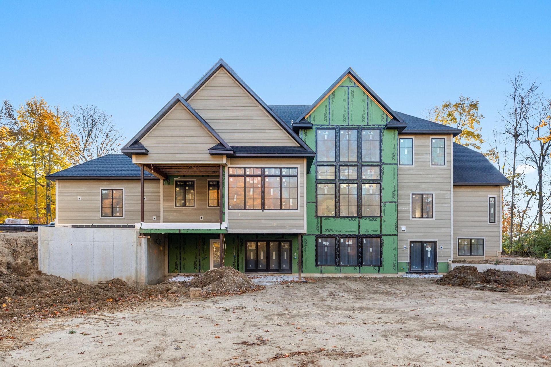 New house under construction with beige and green siding and a dirt lot in front