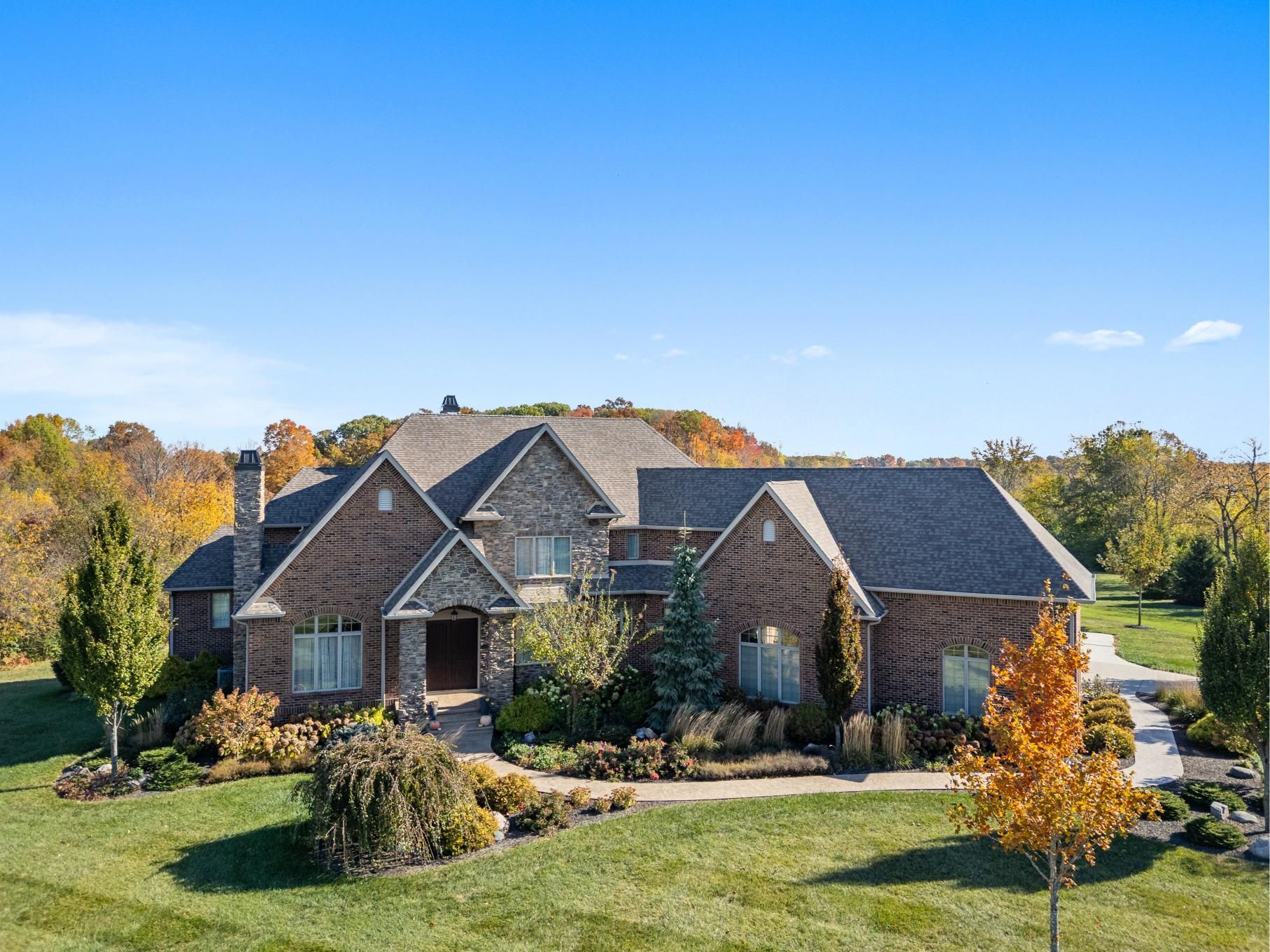 Large stone house with dark roof on a landscaped lawn under a bright blue sky