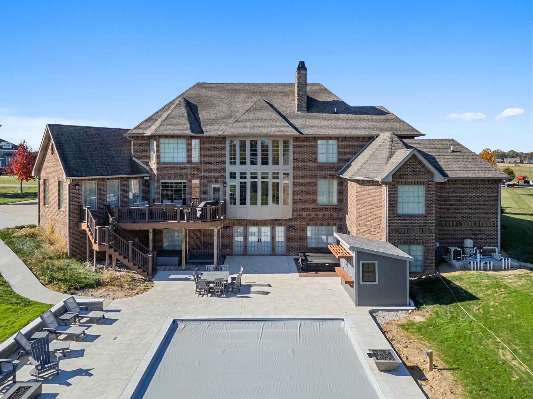 Large brick suburban house with a balcony, deck, and driveway under a clear blue sky