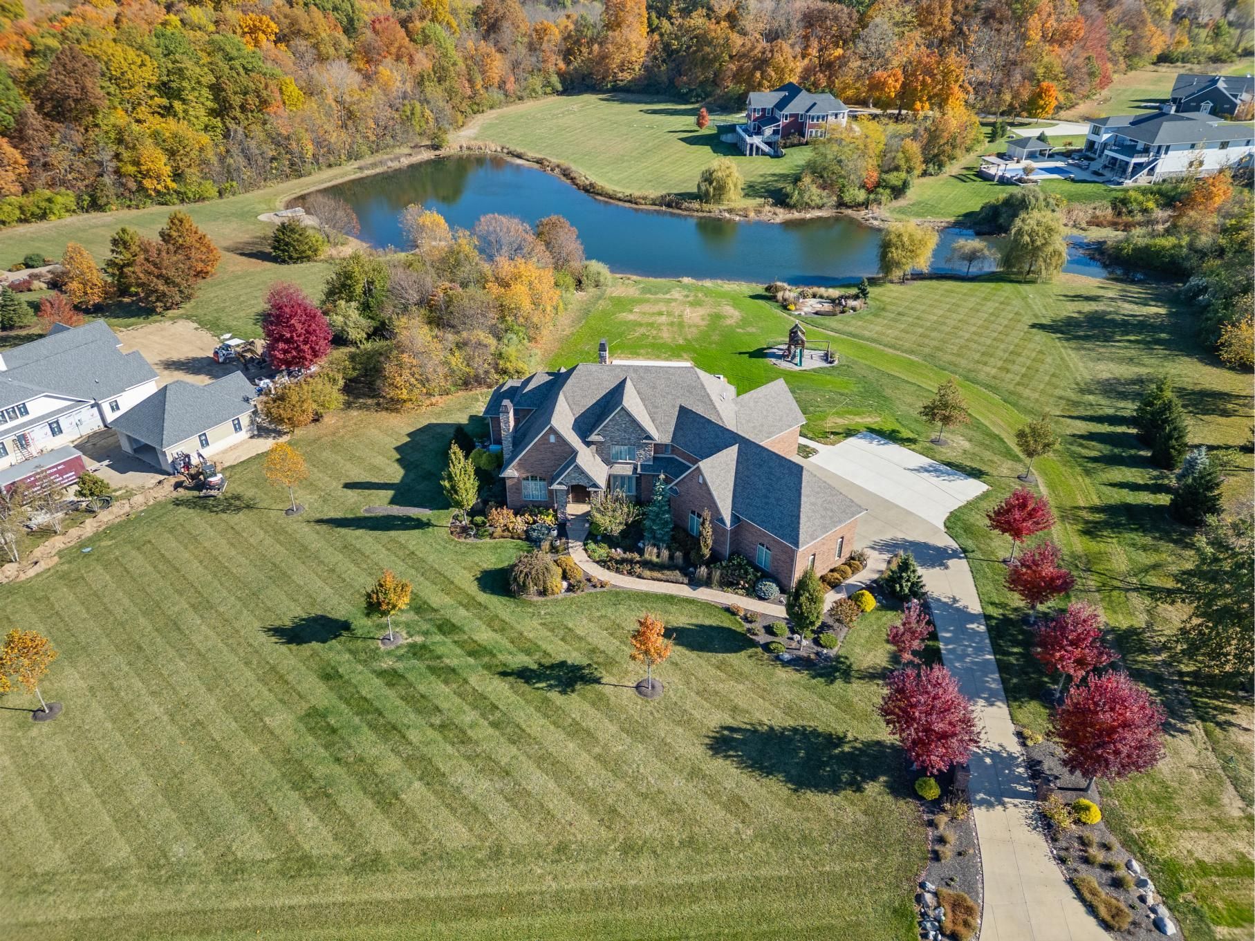 Aerial view of a large house with manicured lawn, trees, and a pond in a colorful autumn neighborhood