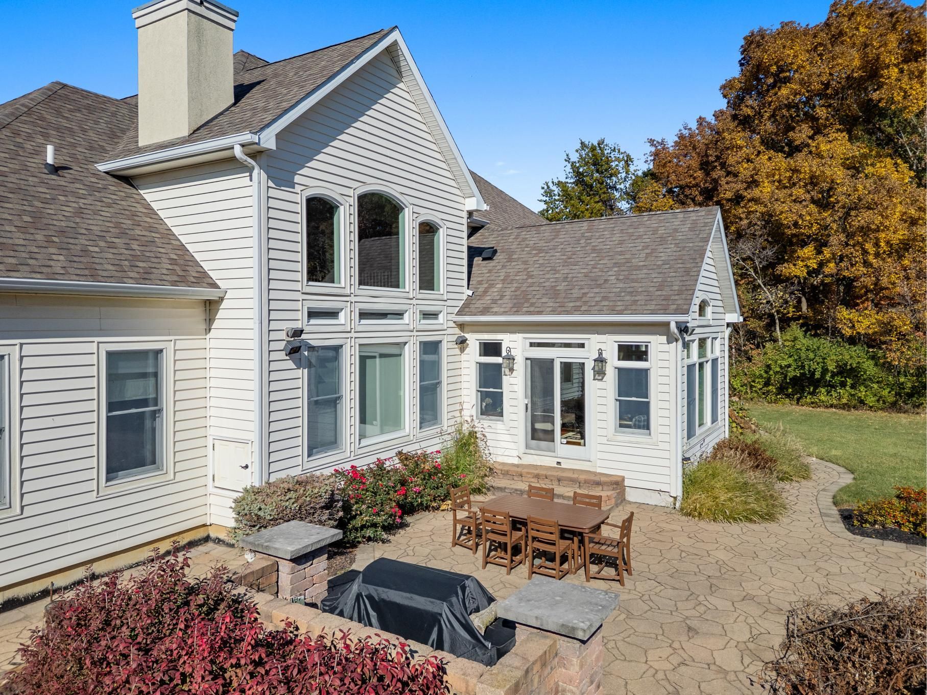 Modern white house with stone patio, outdoor dining table, and autumn trees in the yard