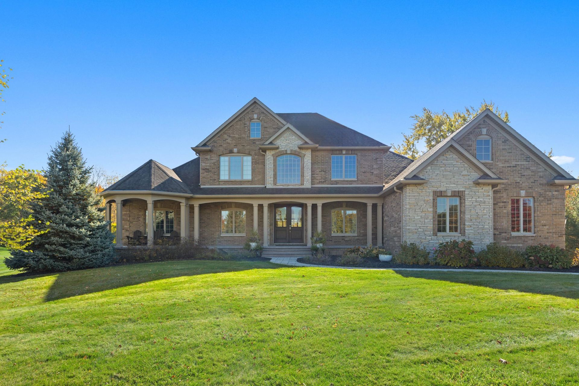 Large two-story stone and brick suburban house with a front porch and green lawn