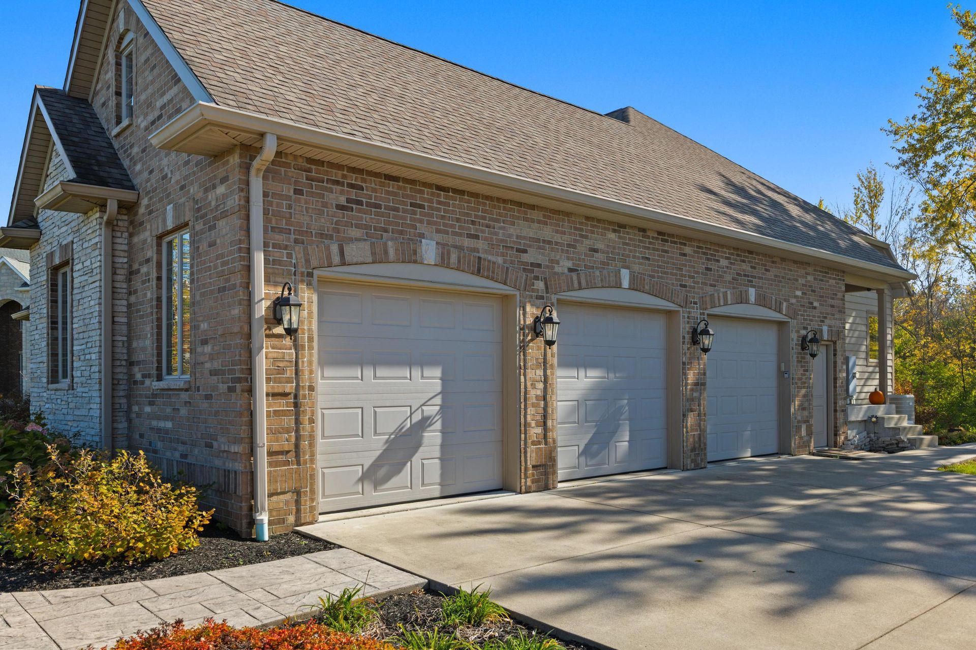Brick house exterior with three garage doors and a concrete driveway in bright sunlight