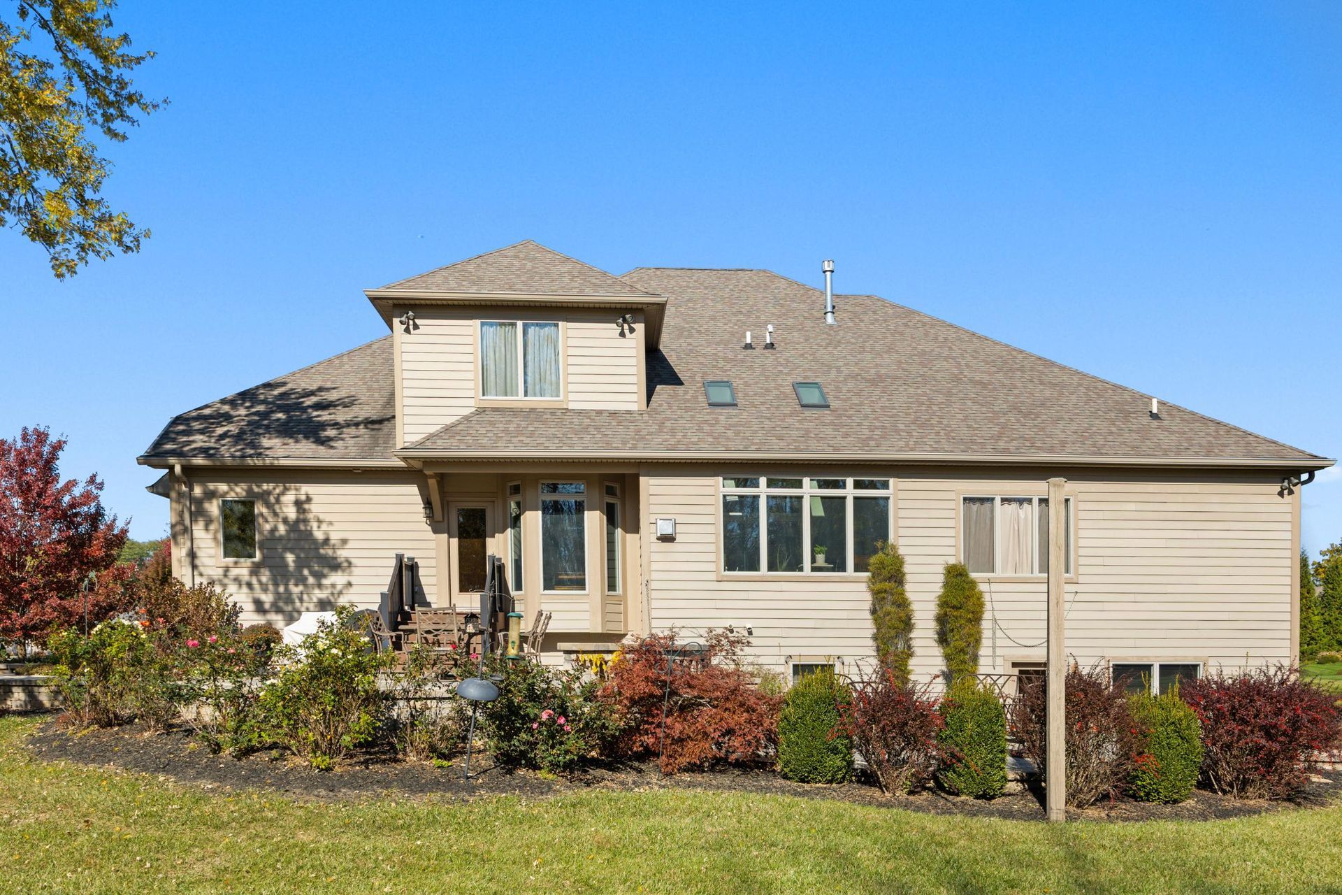 Suburban beige house with a front porch, lawn, shrubs, and a blue sky background