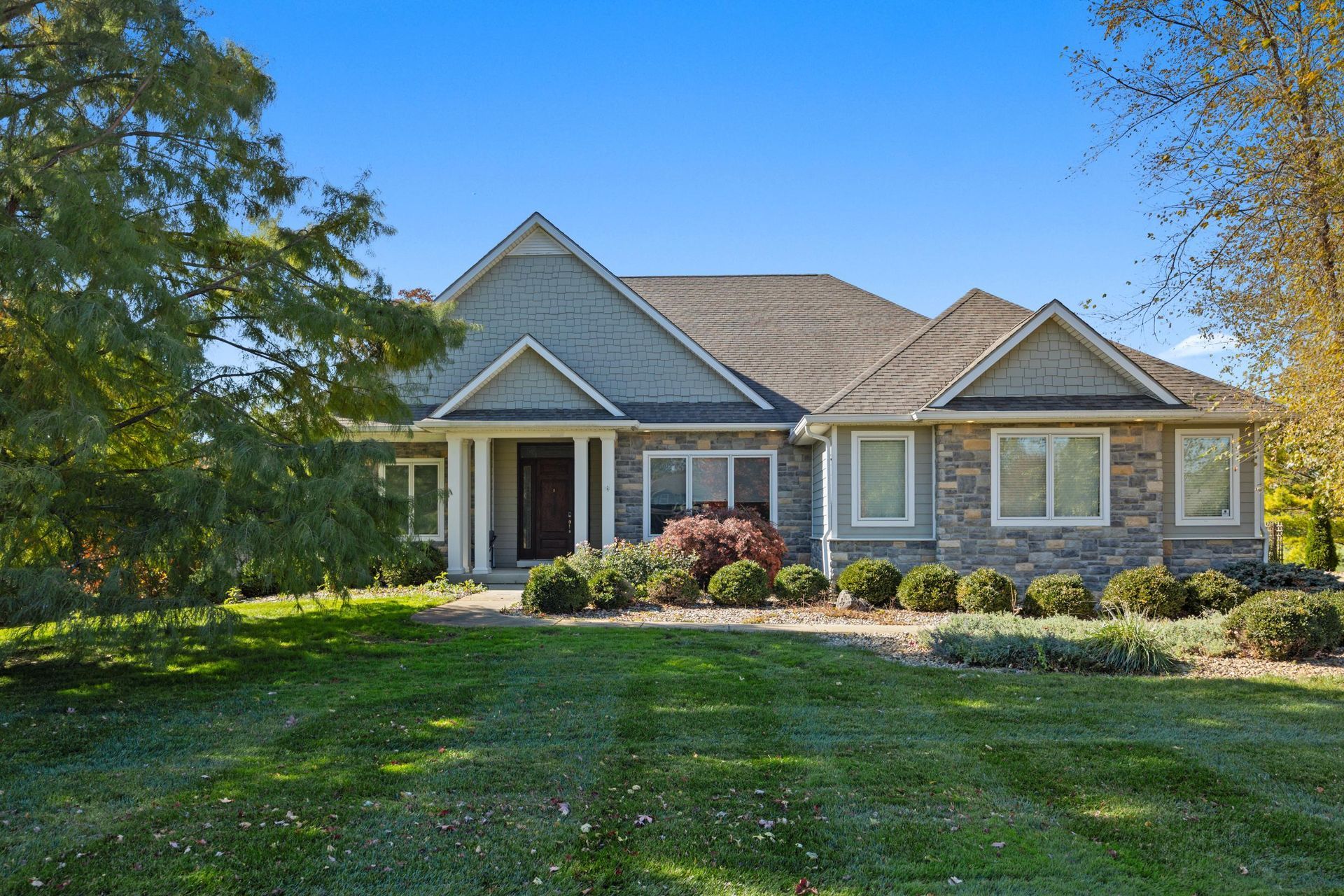 Single-story suburban house with stone facade, front porch, and landscaped lawn under sunny skies