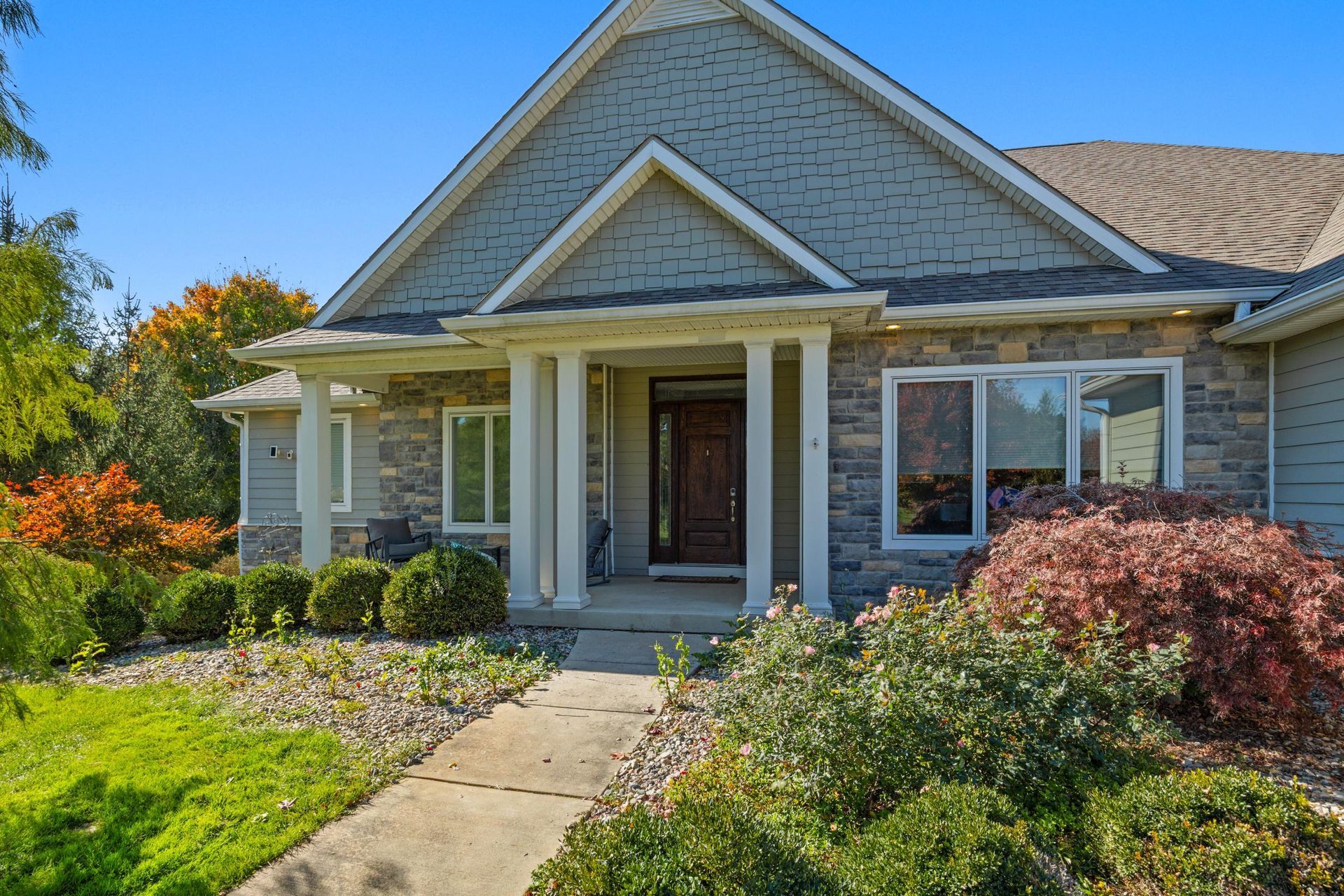 Suburban house with gray siding, front porch, and landscaped garden under a clear sky