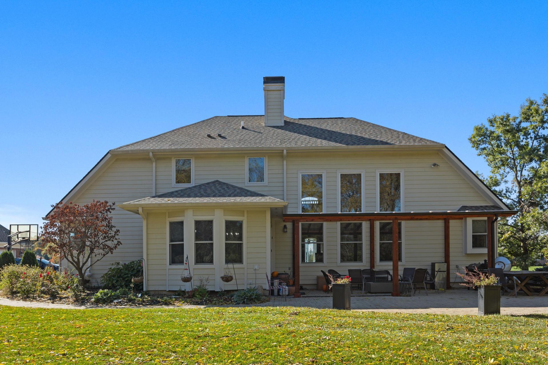 Two-story cream house with porch and chimney under a blue sky, surrounded by a grassy yard