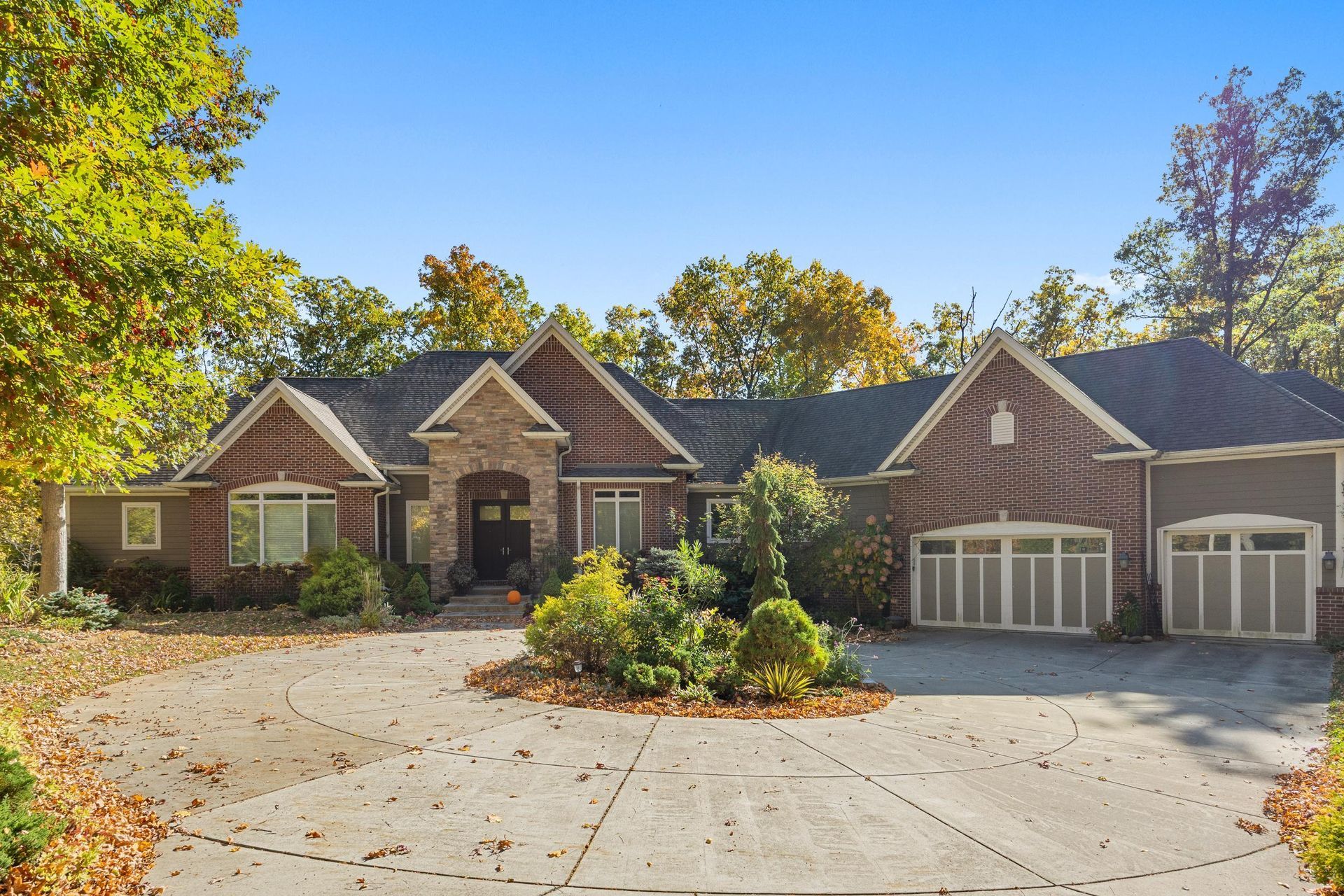 Large brick house with a three-car garage and a curved driveway surrounded by autumn trees