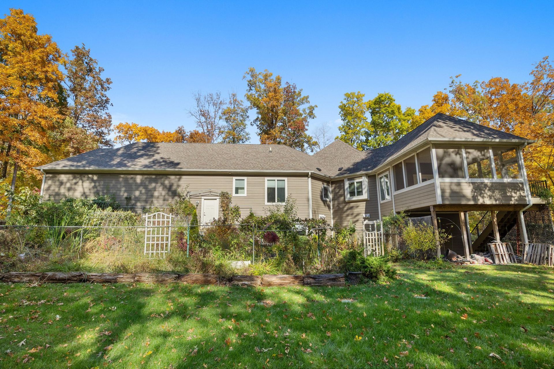 Suburban house with screened porch, autumn trees, and a green lawn under a clear blue sky