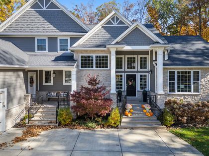 Suburban house with gray siding, white trim, and a front walkway lined by autumn shrubs