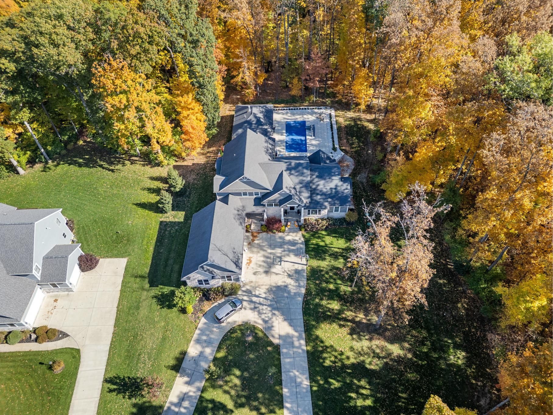 Aerial view of a house with a long driveway, surrounded by autumn trees and lawn.