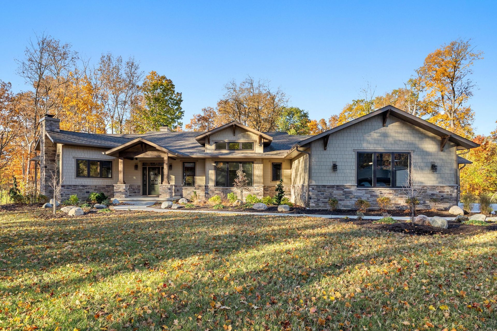 Single-story stone house with autumn trees and a grassy front yard under a clear blue sky