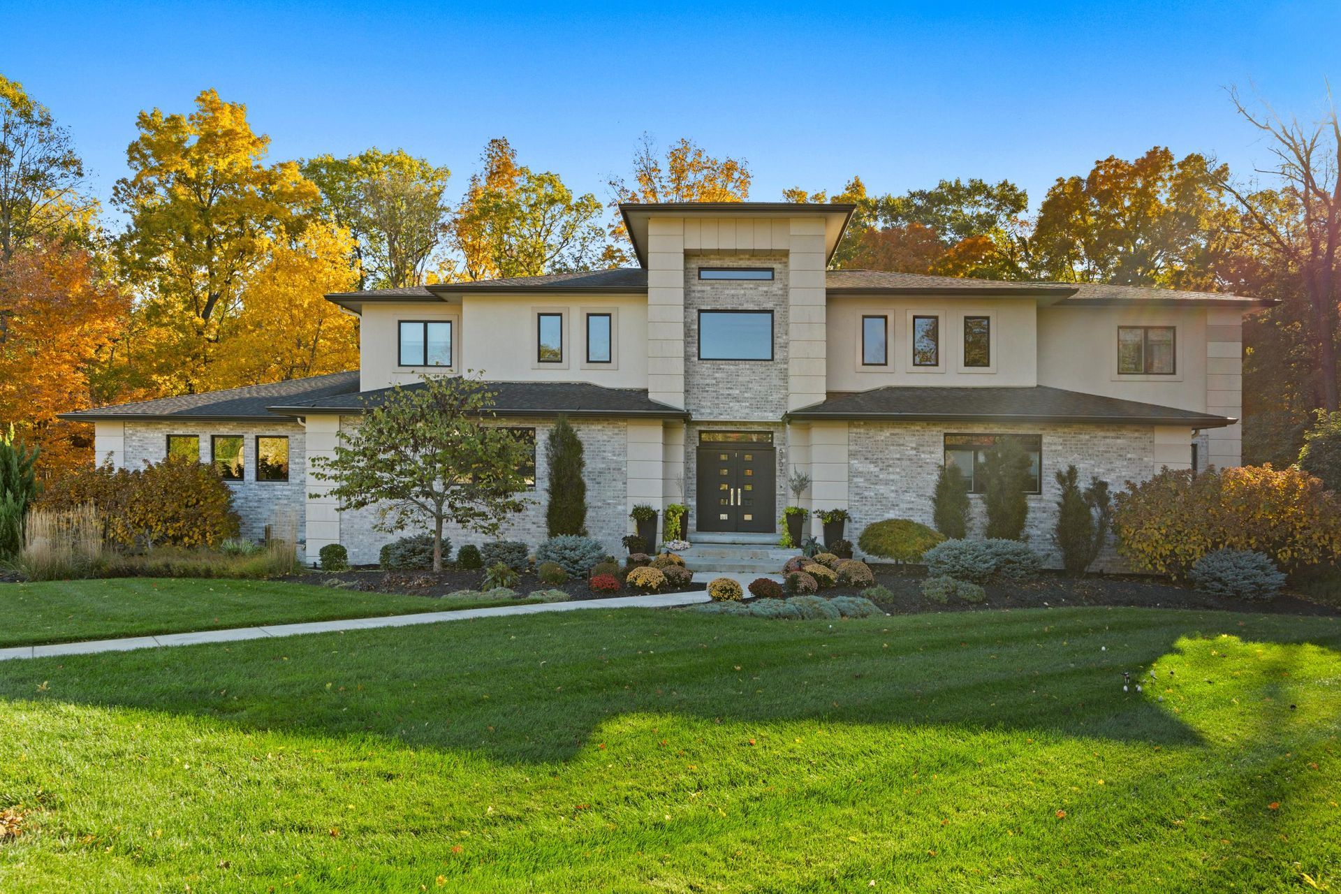 Large modern two-story house with stone siding, green lawn, and autumn trees at sunset