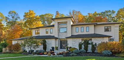 Suburban house with gray siding, white trim, and a front walkway lined by autumn shrubs