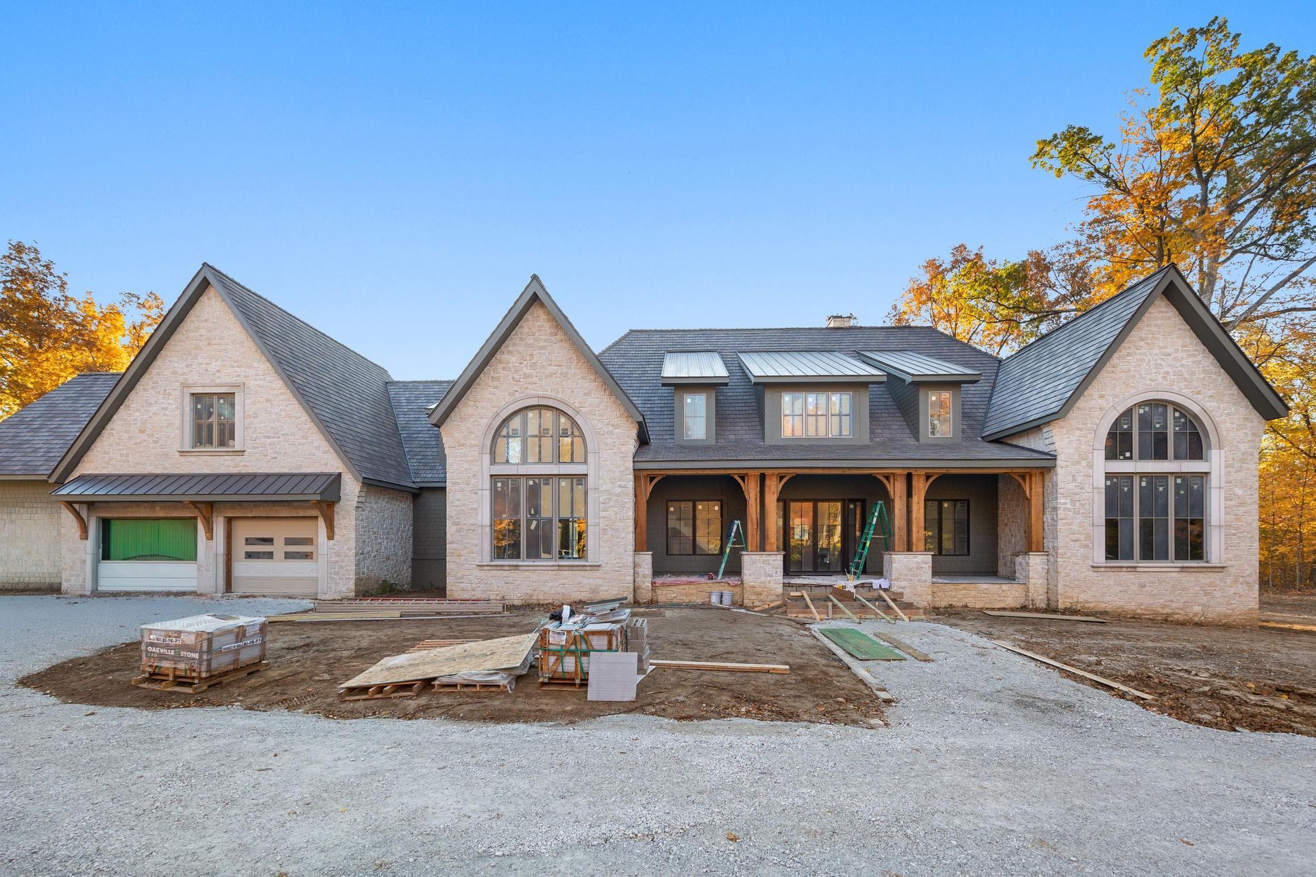 Large stone suburban house under construction with unfinished front yard and gravel driveway