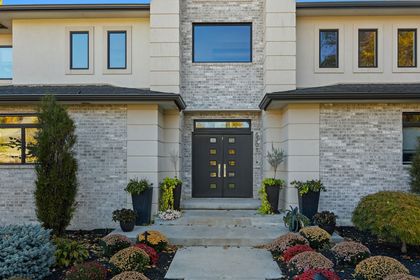 Modern two-story house entrance with stone facade, dark front door, and landscaped front yard