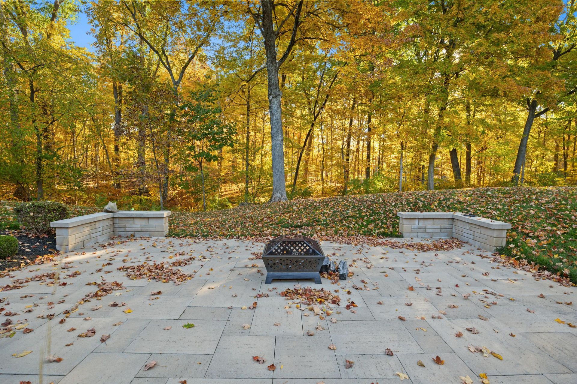 Patio with a fire pit and stone benches overlooking an autumn forest