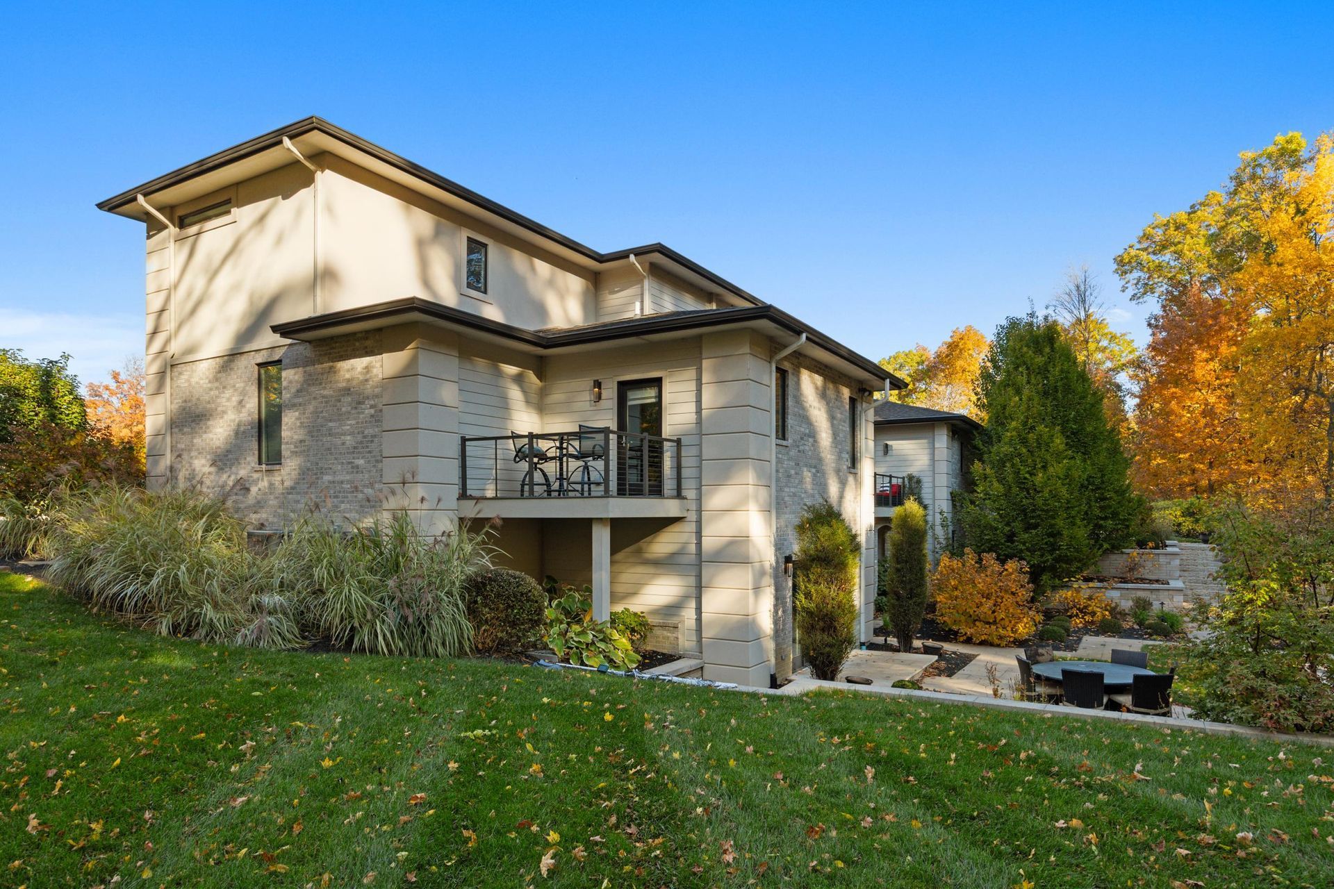Two-story beige house with a balcony and autumn trees in the yard