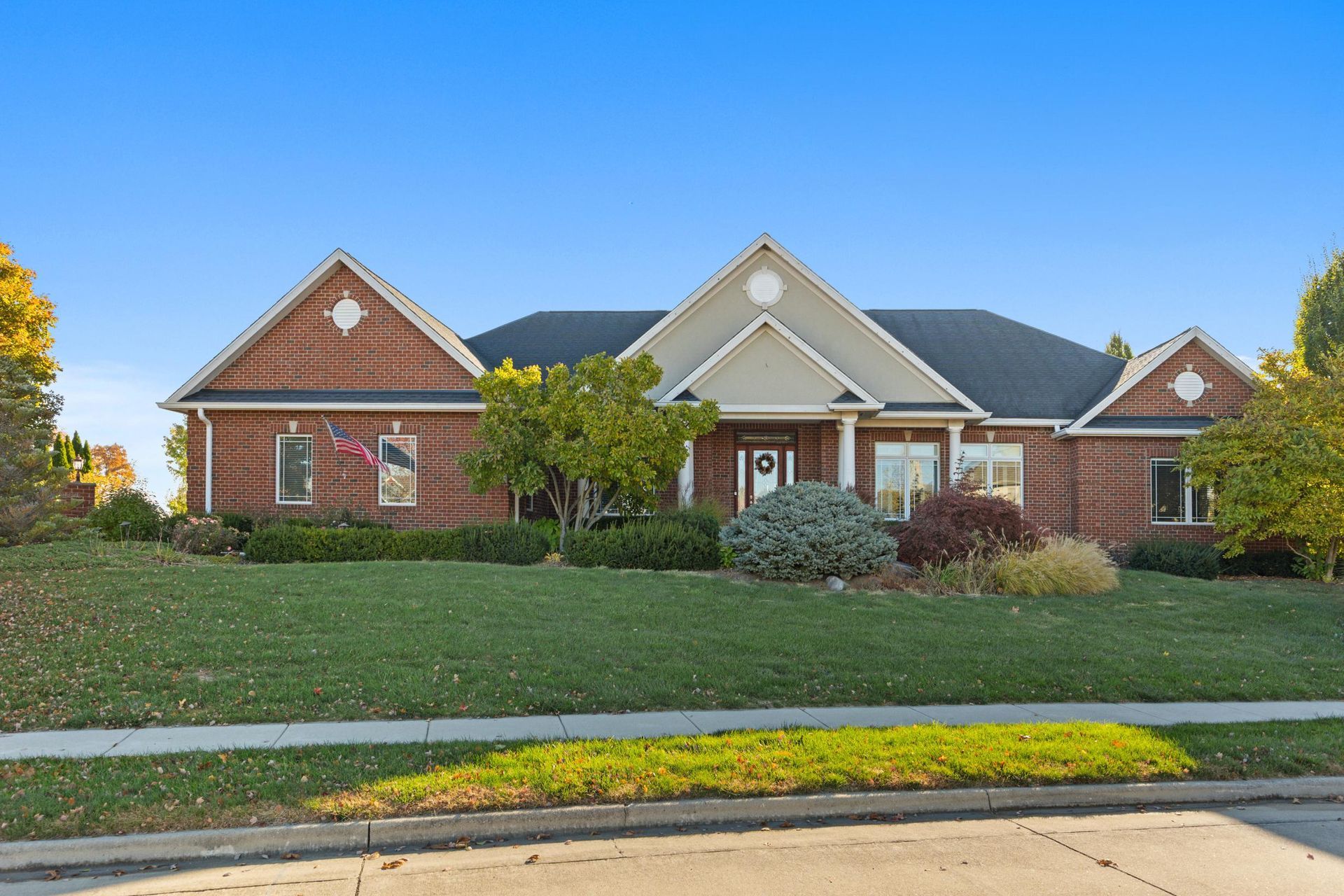 Brick house with green lawn and shrubs under a clear blue sky