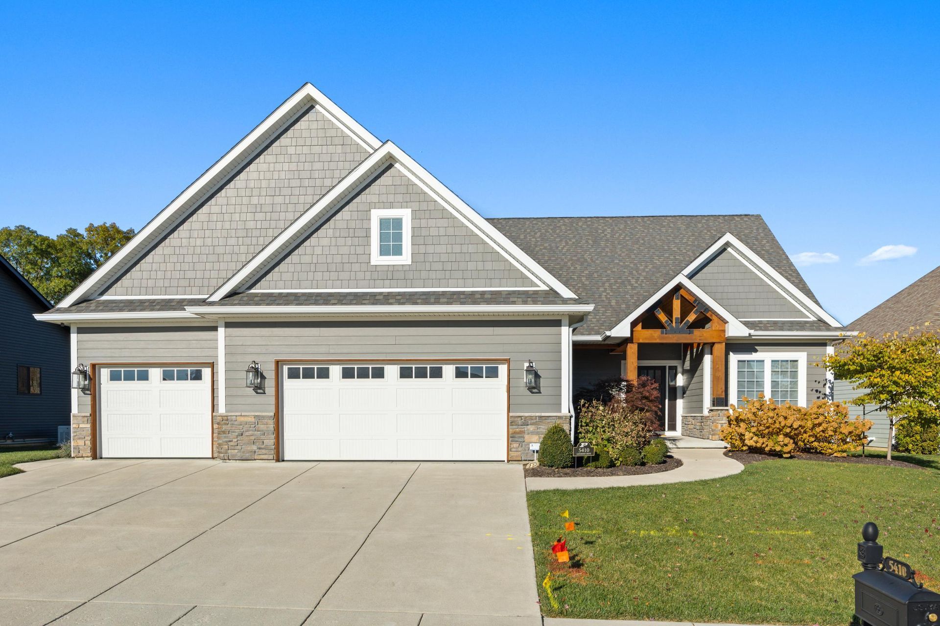Modern gray suburban house with three-car garage, front porch, and manicured lawn under a clear blue sky