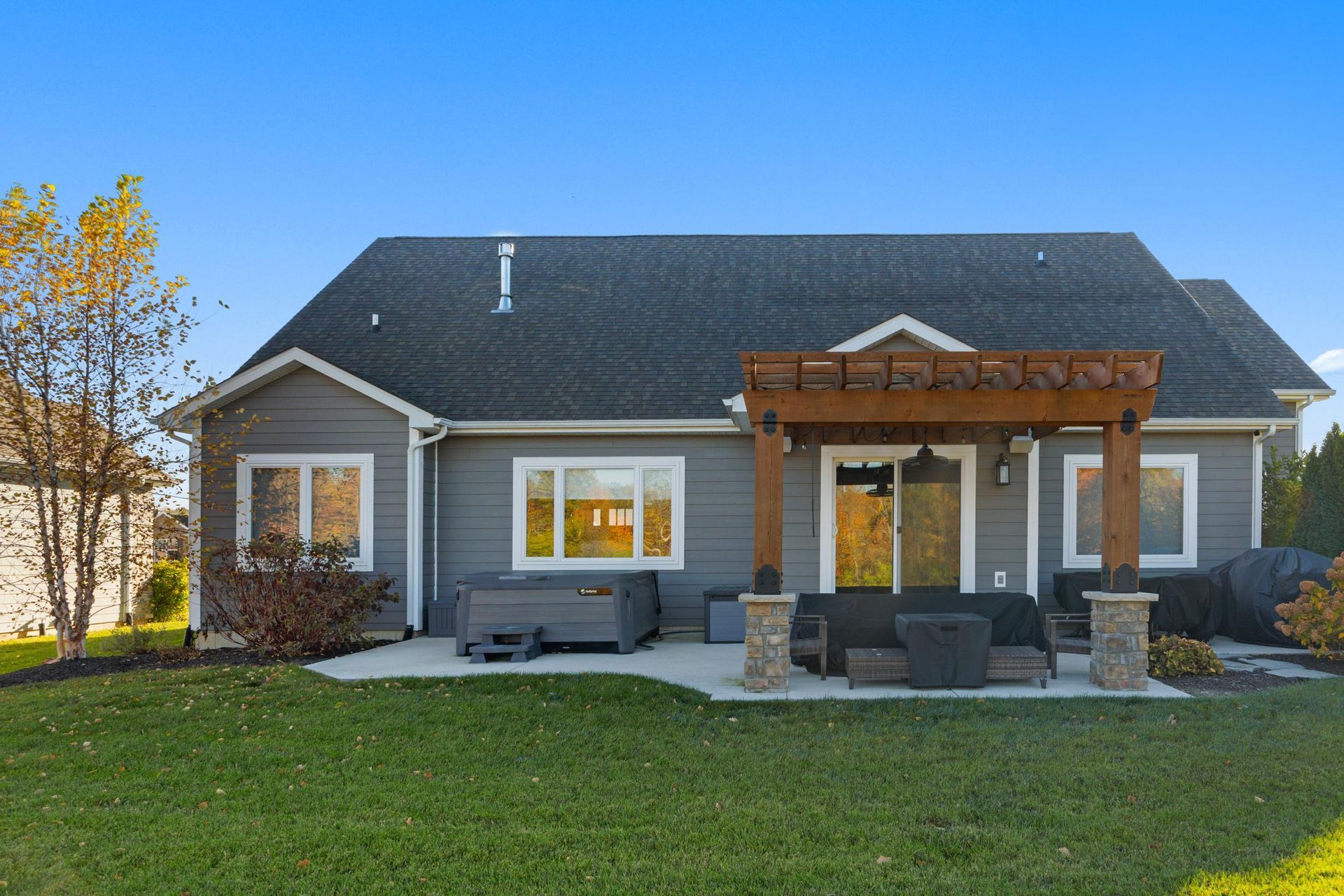 Gray suburban house with a covered patio, stone columns, and a green lawn in front