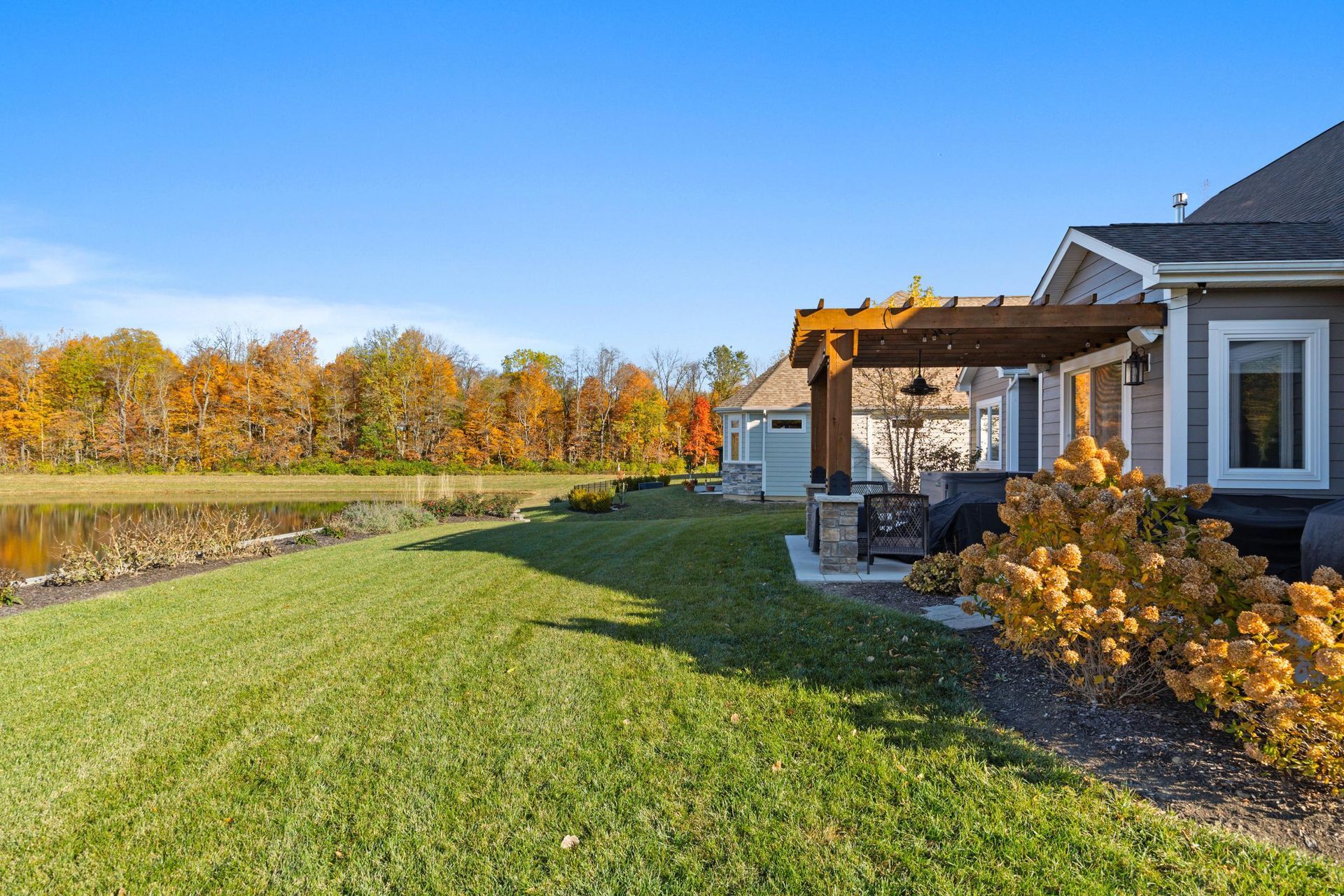 Suburban backyard with green lawn, patio, and autumn trees under a clear blue sky