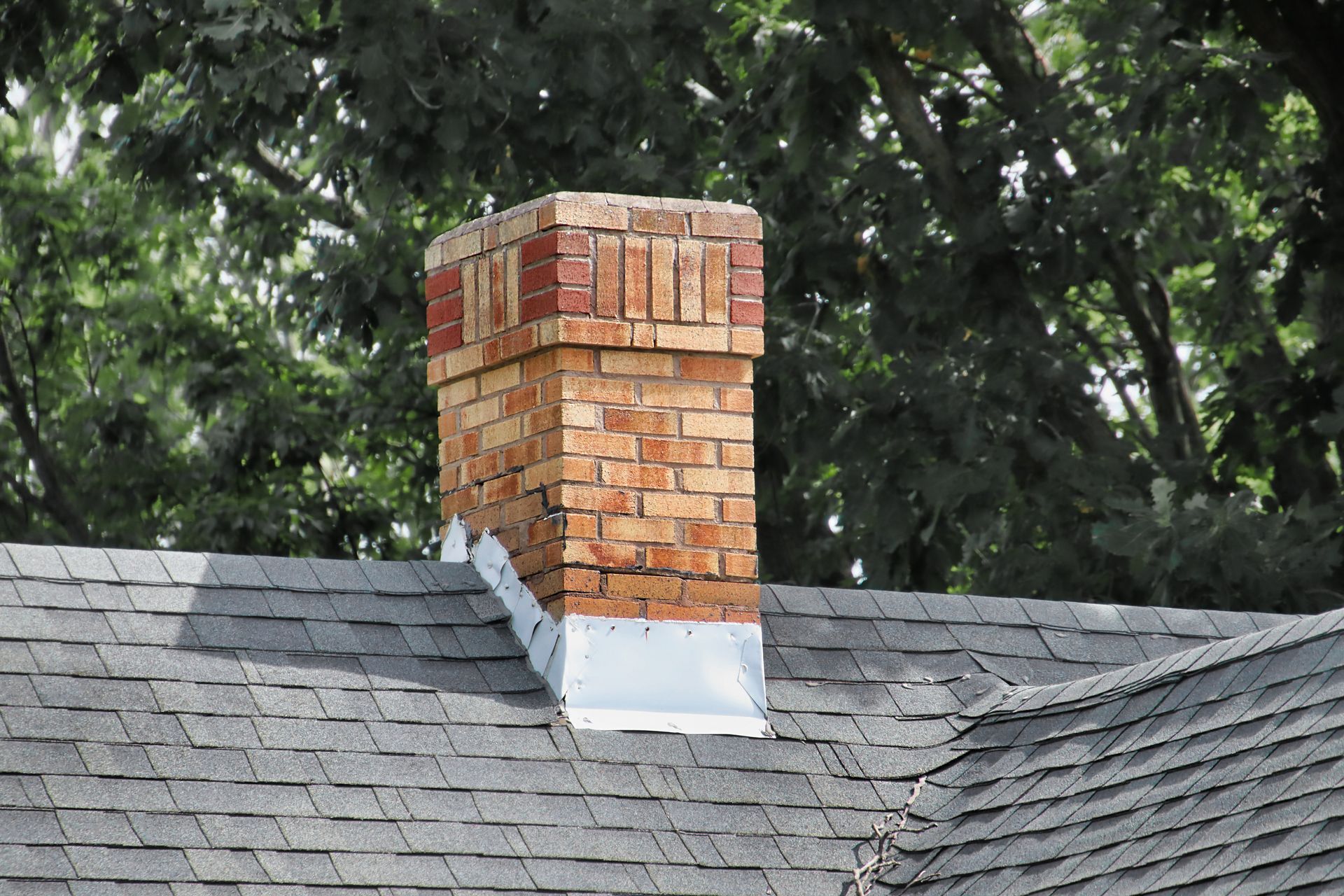 A brick chimney and two skylights installed on a gray asphalt shingle roof.