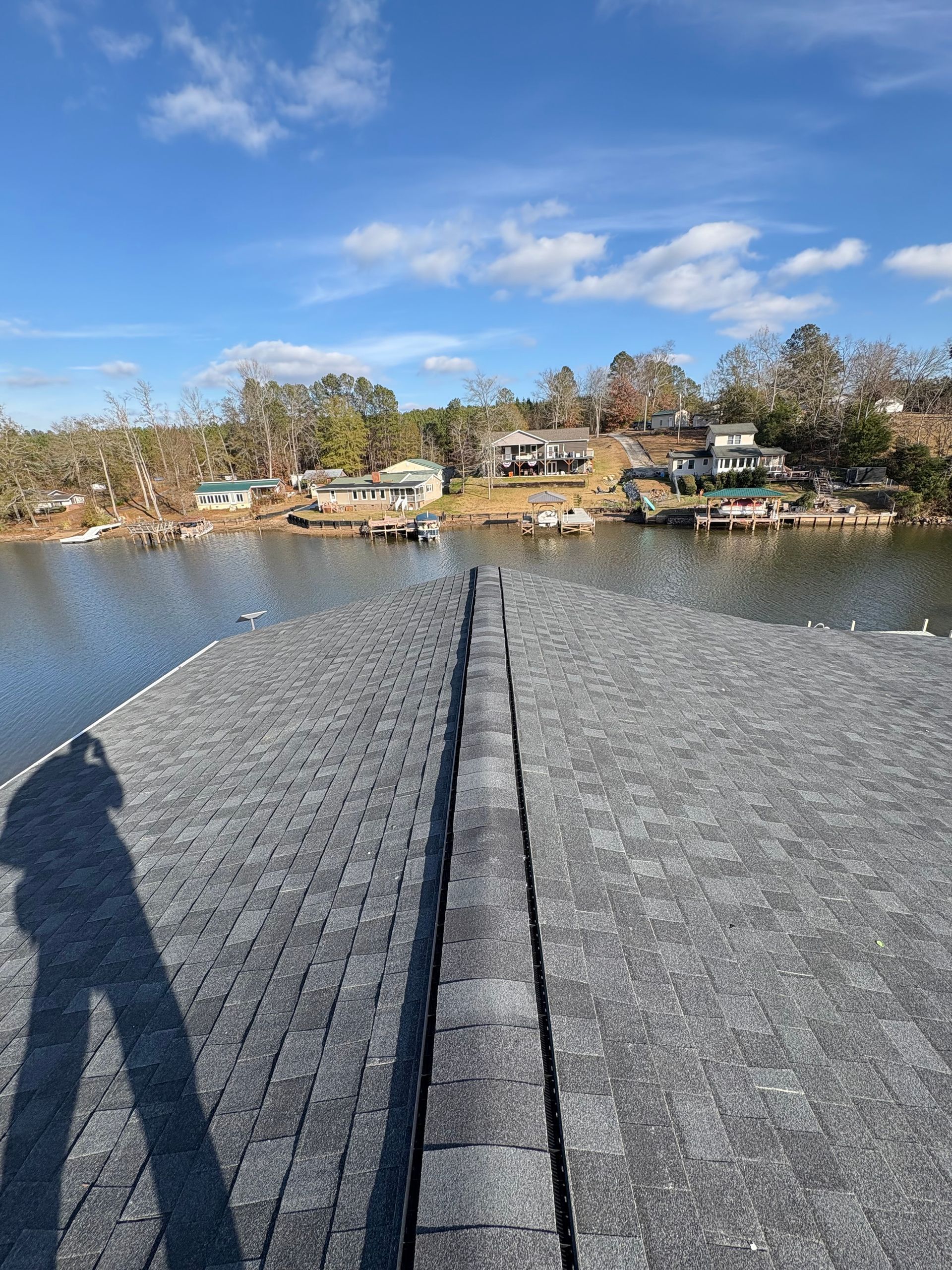 A professional roofer hammering a dark asphalt shingle onto a sloped residential roof on a sunny day. A professional roofer hammering a dark asphalt shingle onto a sloped residential roof on a sunny day.