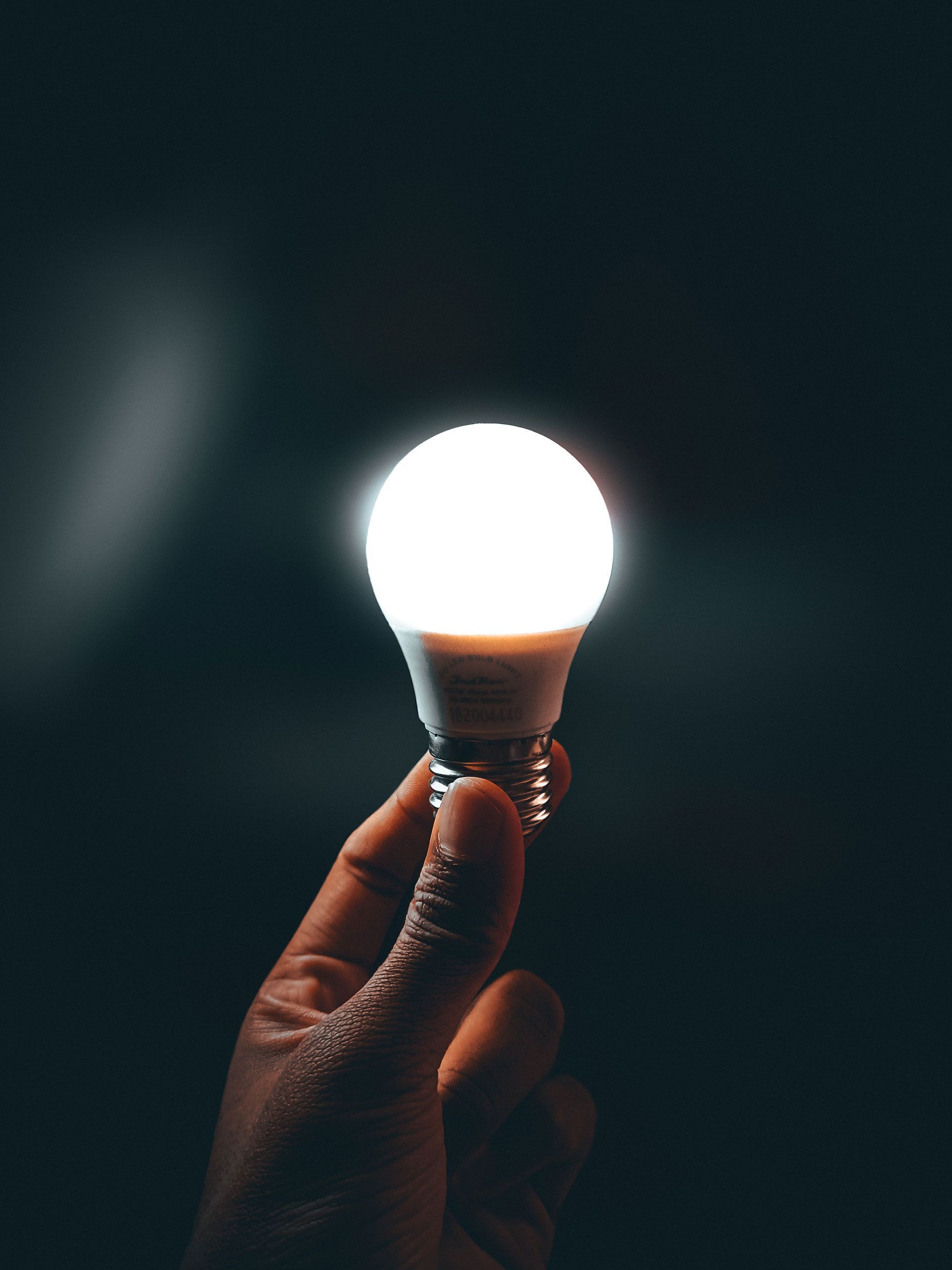 A person is holding a light bulb in their hand in the dark.