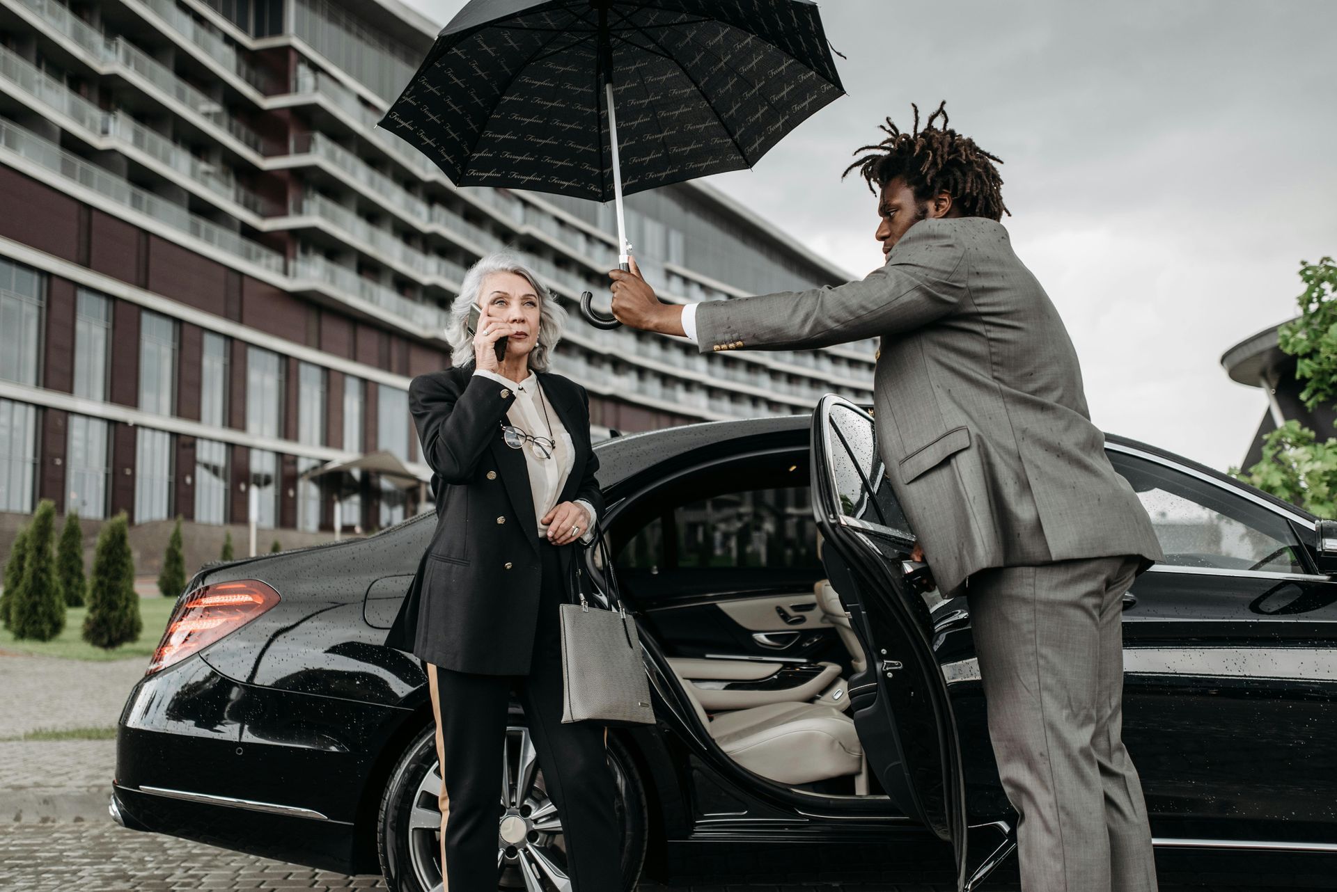 Man opening a black car door for a seated woman in a parking lot, with snow on the ground.