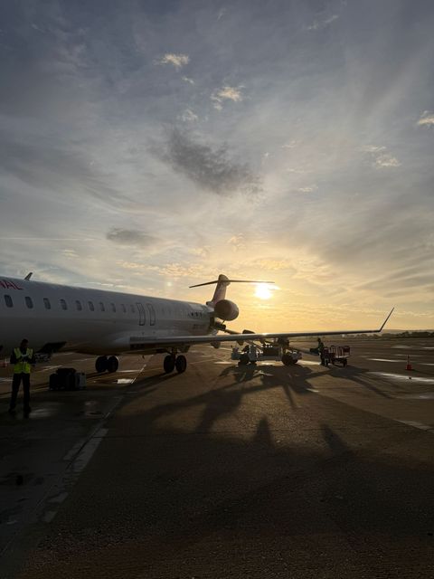 Airplane on runway at sunset, with crew nearby and long shadows across the tarmac