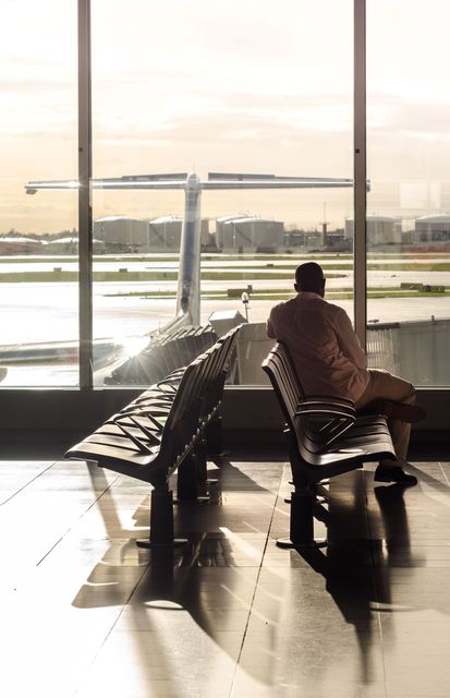 Person sitting on an airport bench facing the runway at sunset